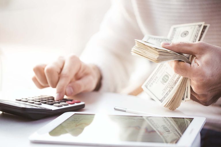 Hands counting us dollars with calculator and digital tablet